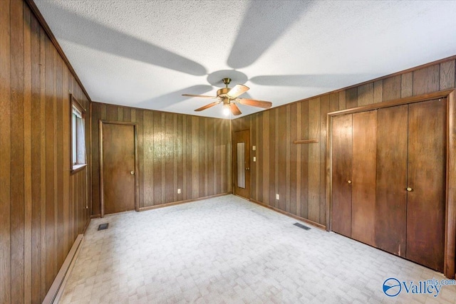 unfurnished bedroom with ceiling fan, wooden walls, a textured ceiling, and a baseboard heating unit