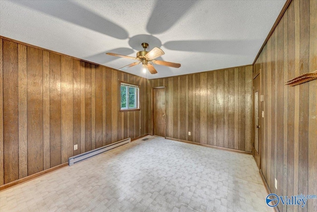 spare room with a textured ceiling, a baseboard radiator, wooden walls, and ceiling fan