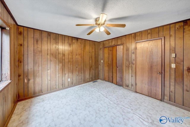 unfurnished bedroom with multiple closets, ceiling fan, a textured ceiling, and wood walls