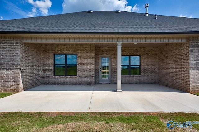 back of house with brick siding, a shingled roof, and a patio