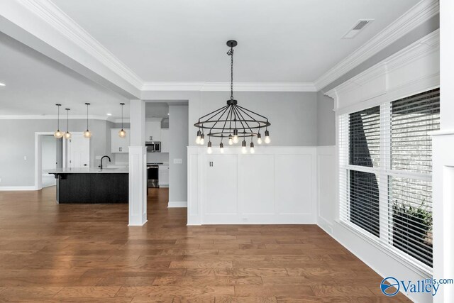 unfurnished dining area with a sink, a chandelier, crown molding, and dark wood finished floors