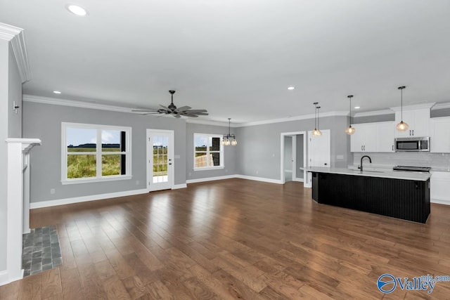 unfurnished living room featuring recessed lighting, dark wood-style flooring, ornamental molding, ceiling fan with notable chandelier, and baseboards