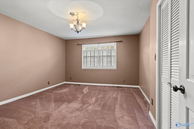 carpeted spare room with a textured ceiling and a chandelier