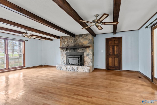 unfurnished living room with beam ceiling, a stone fireplace, ceiling fan, and light hardwood / wood-style floors