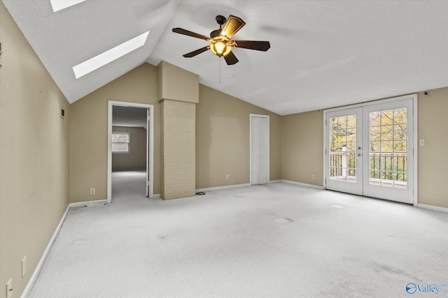 unfurnished living room with ceiling fan, french doors, light carpet, and lofted ceiling with skylight