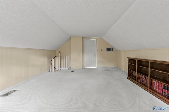 bonus room featuring a textured ceiling, wooden walls, carpet floors, and lofted ceiling