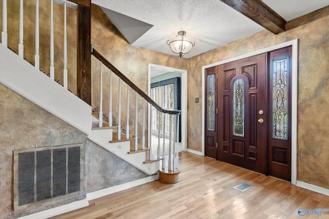foyer entrance with beamed ceiling, wood-type flooring, a textured ceiling, and a notable chandelier
