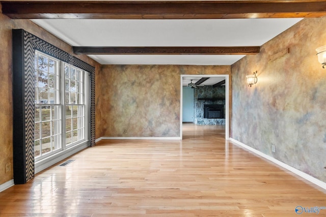 spare room featuring beam ceiling, ceiling fan, a fireplace, and light hardwood / wood-style floors