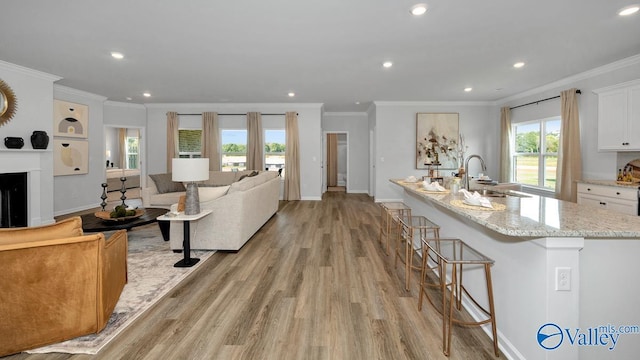 kitchen featuring light stone countertops, ornamental molding, sink, a center island with sink, and white cabinetry