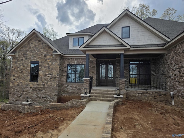 craftsman-style house featuring roof with shingles, brick siding, french doors, and a porch