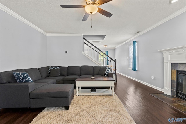 living area featuring crown molding, wood finished floors, a tile fireplace, baseboards, and stairs