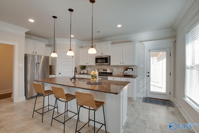 kitchen featuring stainless steel appliances, a wealth of natural light, a kitchen island with sink, a sink, and a kitchen bar