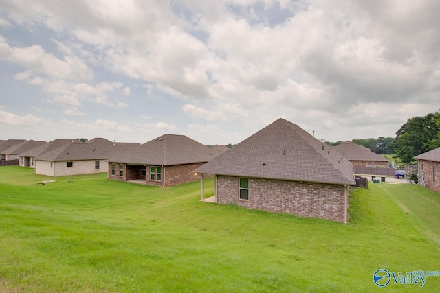 back of property with brick siding, a shingled roof, and a yard