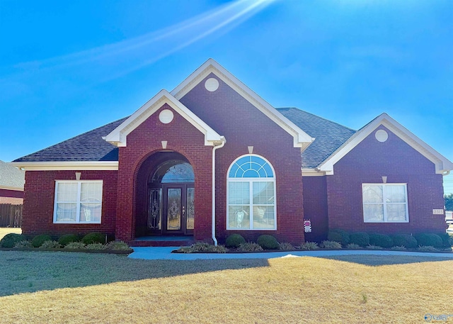 view of front of house with brick siding, french doors, a front yard, and roof with shingles