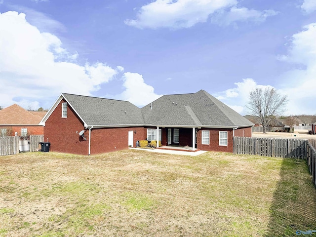 rear view of property with a fenced backyard, a yard, a shingled roof, brick siding, and a patio area