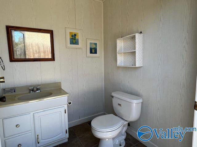 half bathroom with baseboards, toilet, and vanity
