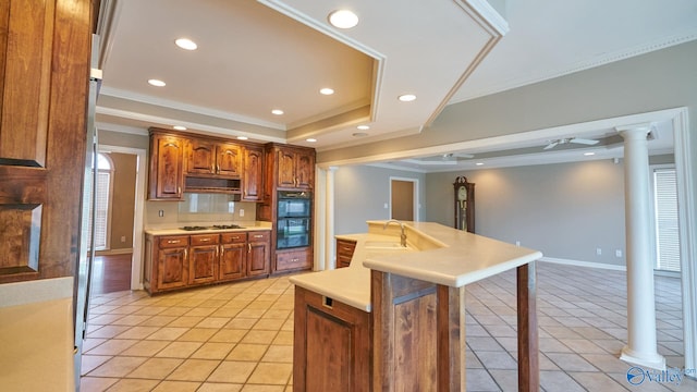 kitchen with light tile patterned flooring, a tray ceiling, ornamental molding, decorative columns, and a kitchen breakfast bar