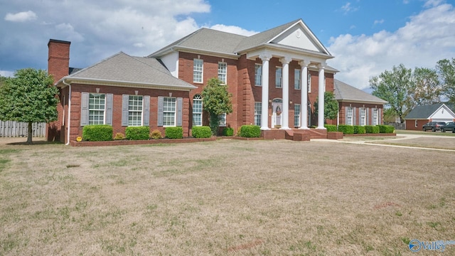greek revival inspired property featuring brick siding, roof with shingles, a chimney, and a front yard