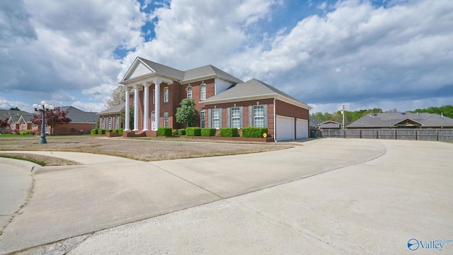greek revival inspired property with concrete driveway, brick siding, fence, and a garage