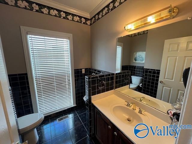 bathroom with toilet, vanity, tile walls, tile patterned floors, and ornamental molding