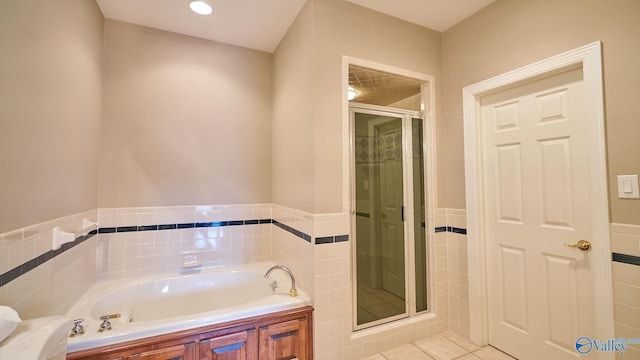 bathroom with a stall shower, a bath, tile walls, a wainscoted wall, and tile patterned flooring