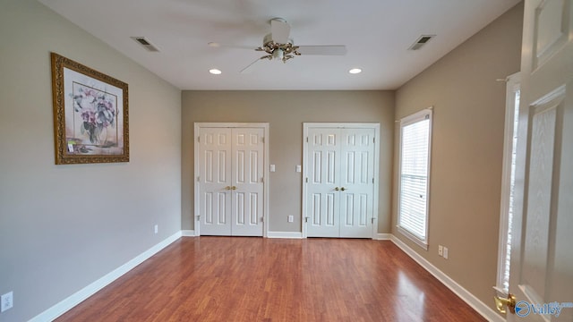 unfurnished bedroom featuring baseboards, wood finished floors, visible vents, and two closets