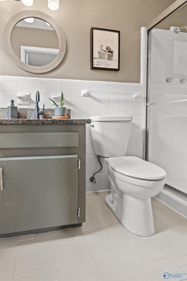 bathroom with tile patterned floors, an enclosed shower, toilet, vanity, and tile walls