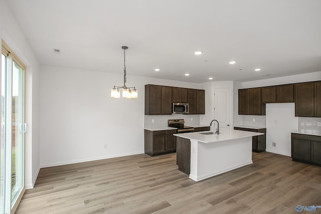 kitchen featuring sink, hanging light fixtures, a kitchen island with sink, stainless steel appliances, and light hardwood / wood-style floors