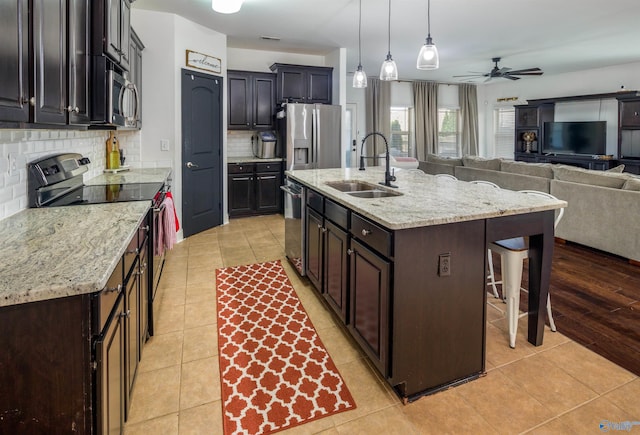 kitchen with light tile patterned floors, stainless steel appliances, a sink, a kitchen bar, and a center island with sink