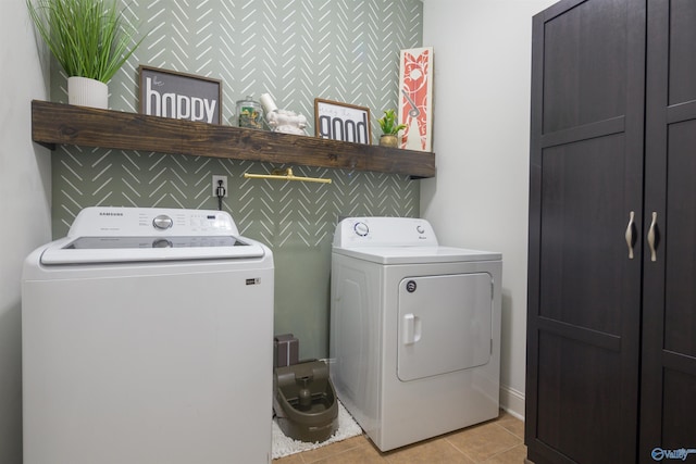 clothes washing area with light tile patterned floors, an accent wall, independent washer and dryer, and cabinet space