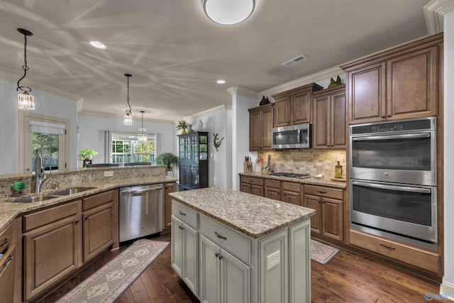 kitchen featuring sink, appliances with stainless steel finishes, hanging light fixtures, a kitchen island, and dark wood-type flooring