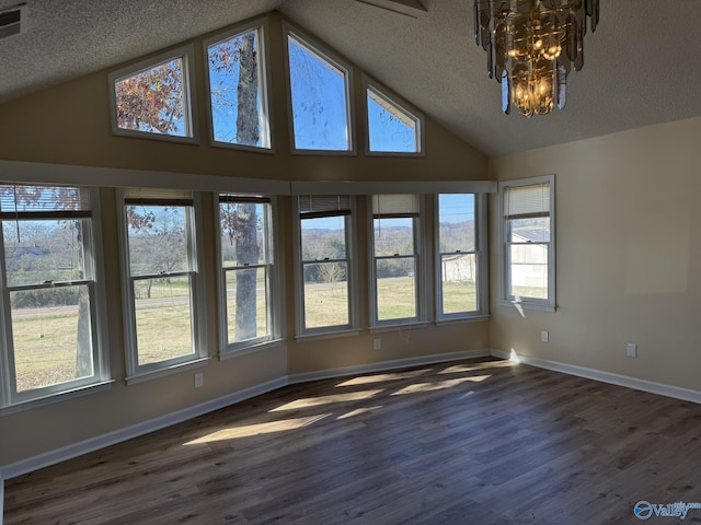 unfurnished room with a chandelier, a textured ceiling, dark hardwood / wood-style floors, and a healthy amount of sunlight