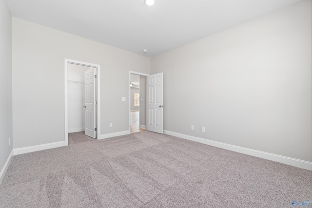 unfurnished bedroom with a walk in closet, a closet, and light colored carpet