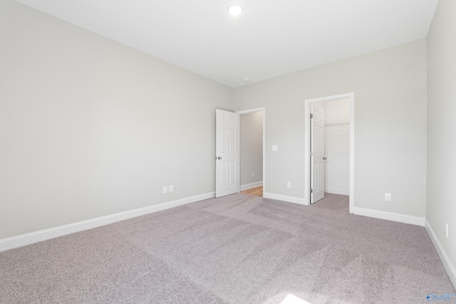 unfurnished bedroom featuring a closet, light carpet, and a walk in closet