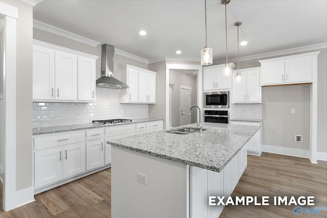 kitchen with wall chimney exhaust hood, stainless steel appliances, a center island with sink, sink, and white cabinets