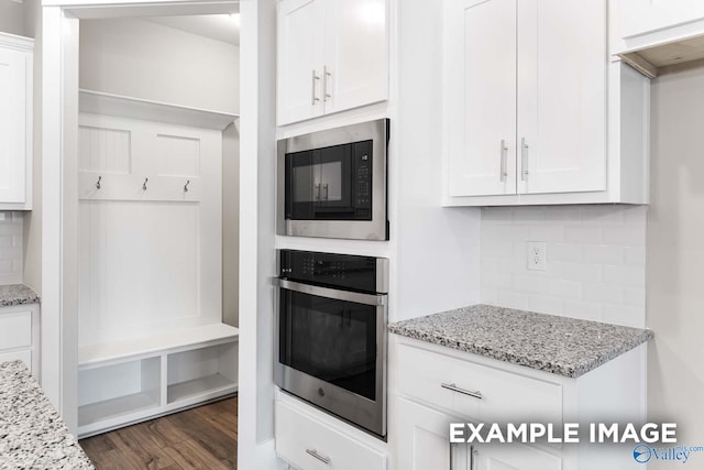 kitchen featuring stainless steel oven, light stone counters, black microwave, and dark hardwood / wood-style flooring