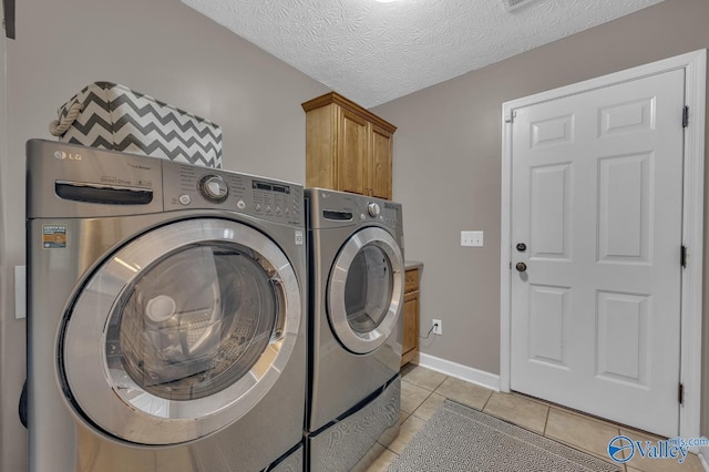 laundry area with a textured ceiling, light tile patterned flooring, cabinet space, and washing machine and dryer