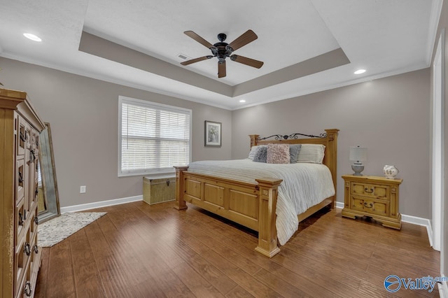 bedroom featuring baseboards, crown molding, visible vents, a raised ceiling, and wood finished floors