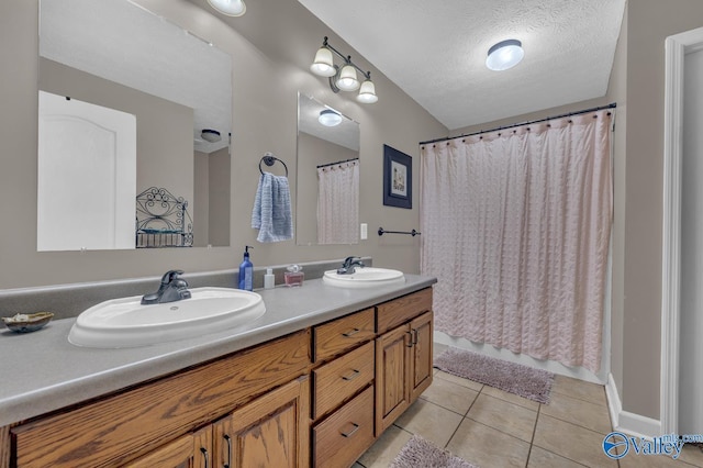 full bathroom featuring a textured ceiling, double vanity, a sink, and tile patterned flooring
