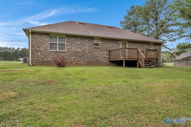 rear view of property with roof with shingles, a yard, brick siding, and a deck