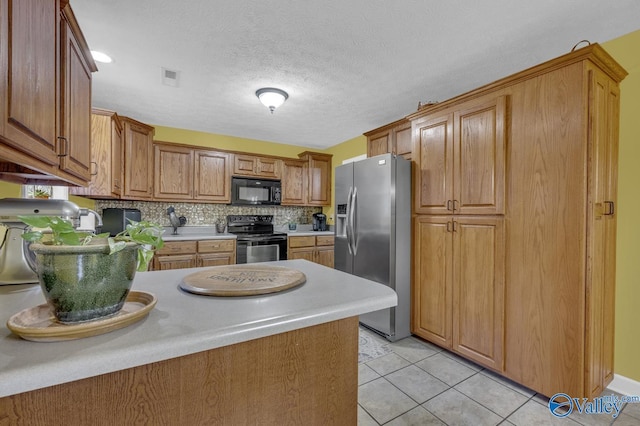 kitchen with light countertops, a peninsula, brown cabinetry, black appliances, and light tile patterned flooring