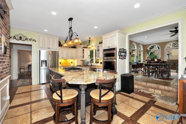 kitchen with cream cabinets, light stone countertops, stainless steel appliances, and decorative light fixtures