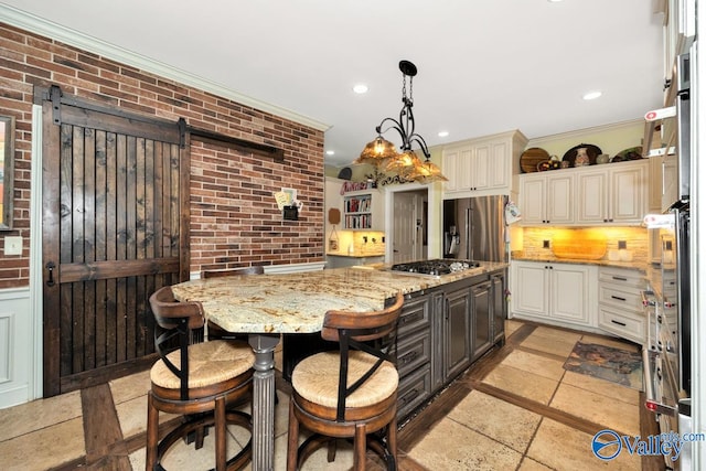 kitchen featuring light stone counters, hanging light fixtures, a barn door, stainless steel appliances, and ornamental molding