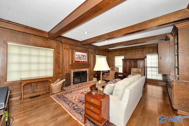 living room with a brick fireplace, wooden walls, beamed ceiling, and hardwood / wood-style floors