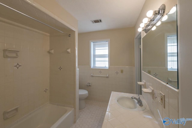 full bathroom featuring toilet, tile patterned flooring, tiled shower / bath, vanity, and tile walls