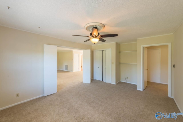 unfurnished bedroom featuring a closet, light carpet, crown molding, a textured ceiling, and ceiling fan