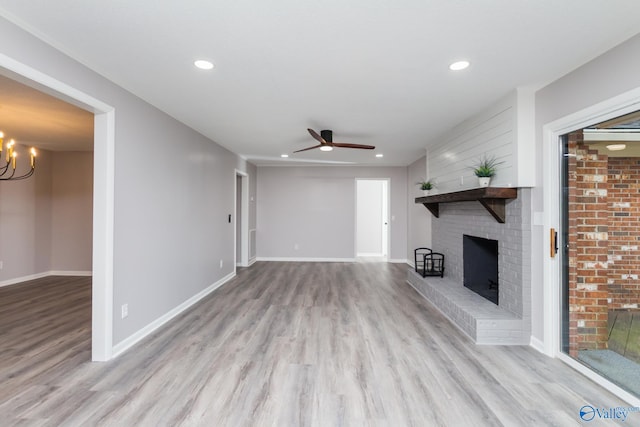 unfurnished living room with ceiling fan with notable chandelier, a fireplace, and light hardwood / wood-style floors