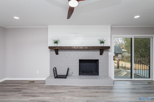 unfurnished living room featuring ceiling fan, ornamental molding, a brick fireplace, and wood-type flooring