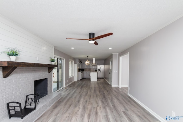 unfurnished living room with a brick fireplace, a textured ceiling, hardwood / wood-style floors, and ceiling fan