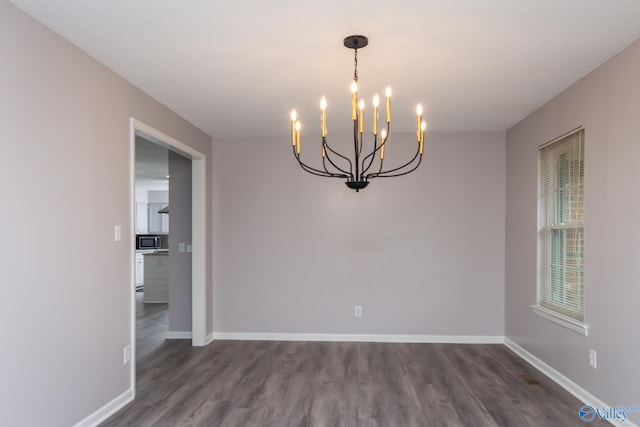 empty room featuring a notable chandelier and dark wood-type flooring